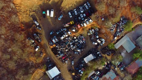 4k top down drone riser with slow spin of a backyard car scrapyard in a caribbean neighborhood during golden hour