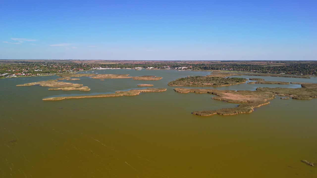 Vista aérea de la ciudad de Velence, Hungría, con islas cubiertas de cañas dispersas por las tranquilas aguas verdes del lago bajo cielos azules y despejados de otoño