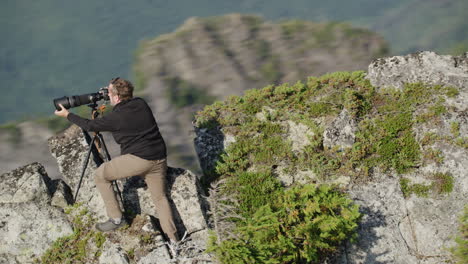 photographer attaches hood to telephoto lens on camera on mountain ridge, tim durkan fast medium tracking helicopter counterclockwise orbit slow motion