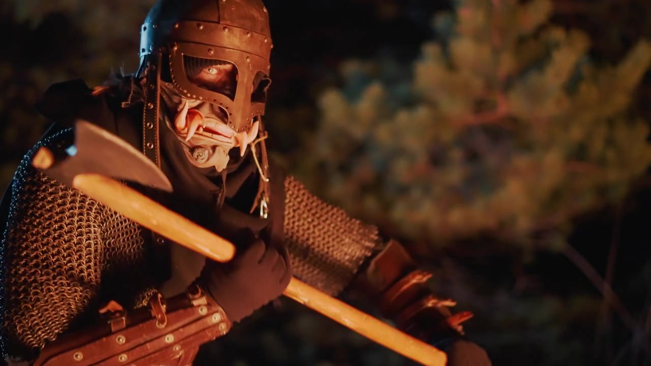 Riveted steel helmet with faceplate and chainmail coif catches warm campfire glow in dark forest while warrior turns slightly and grips wooden pole, creating tense, atmospheric movement and dramatic