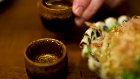 hand pouring sake beside a dish