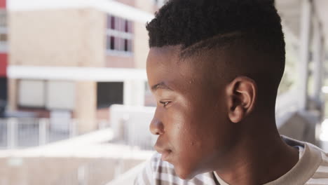 smiling african american teenage boy in school, enjoying break time outside classroom building