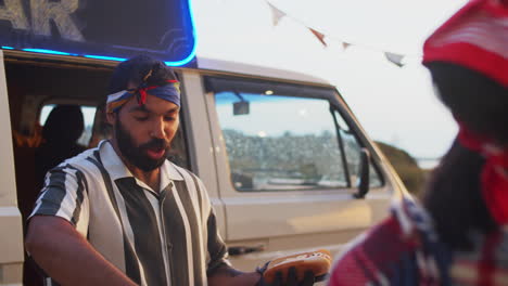 positive food truck seller cooking hot dogs for people at summer festival