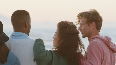 rear view of friends on winter beach watching sunrise together