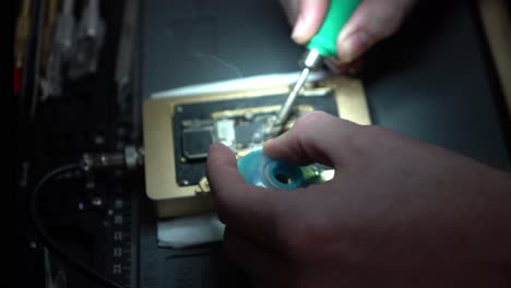 primer plano del hombre microsoldando y reparando una placa en un taller de reparación