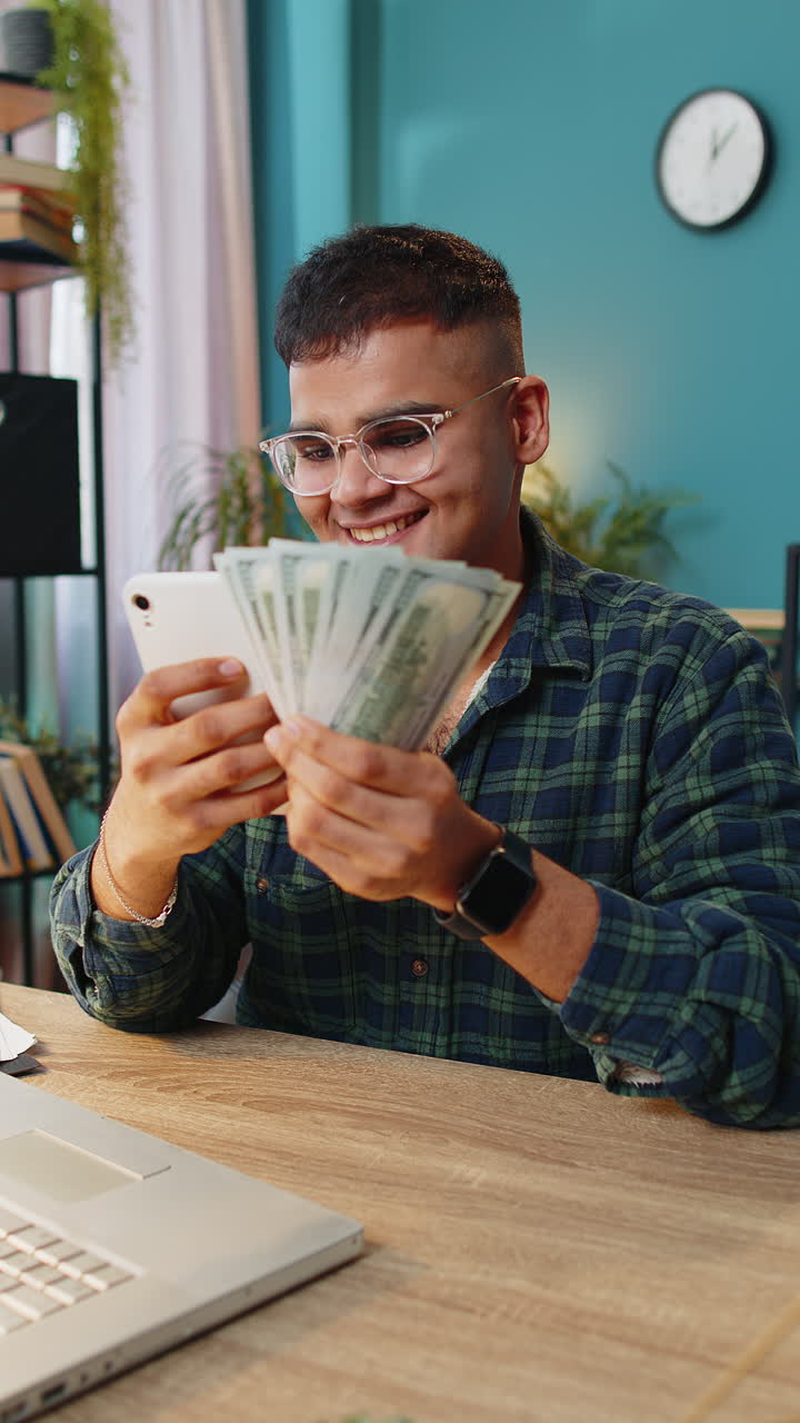 Smiling happy man counting money dollar cash use smartphone income saves lottery win at home
