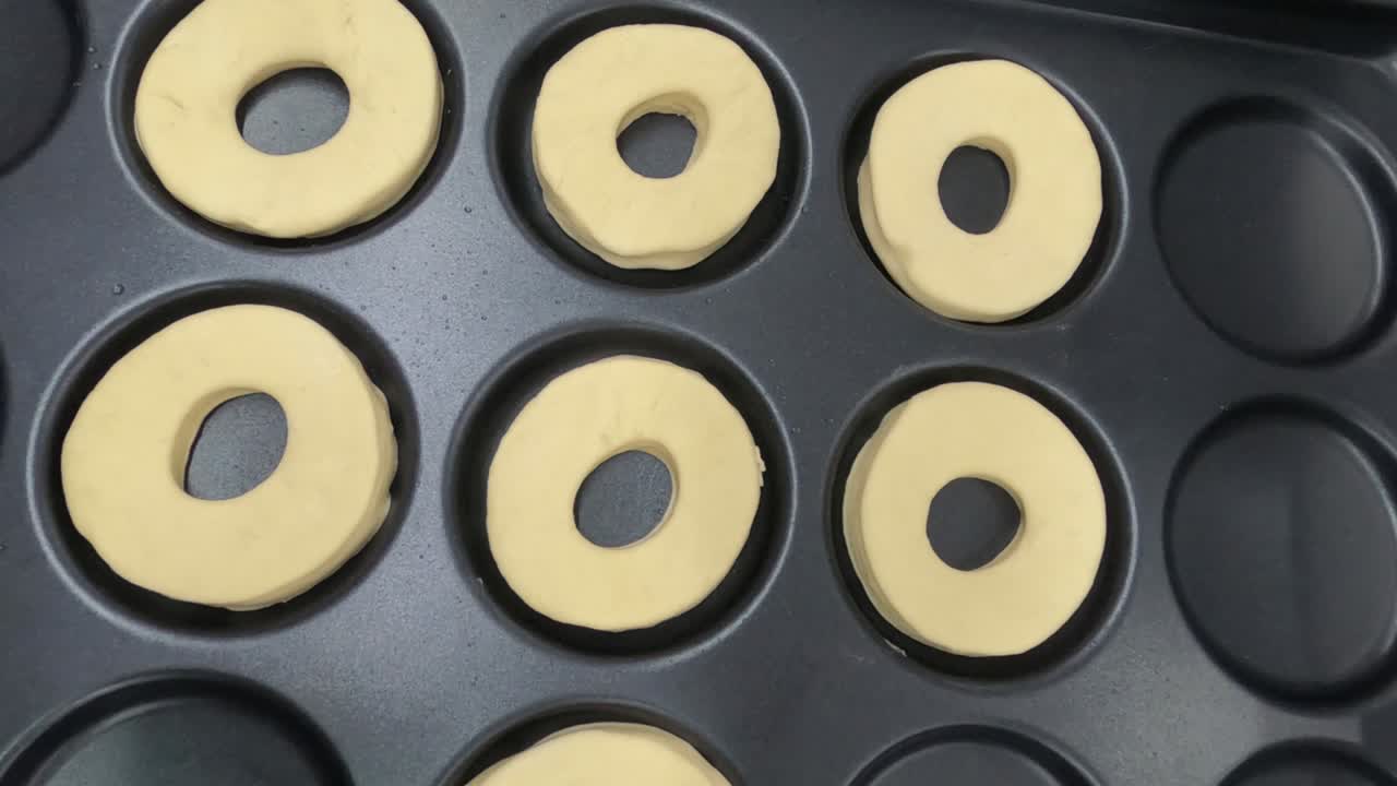 rosquillas crudas en una bandeja negra listas para hornear vista superior movimiento suave 4k videoclip.