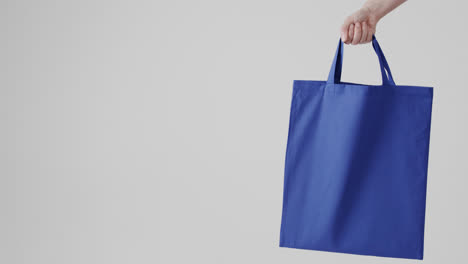 Hand-of-caucasian-woman-holding-blue-bag-on-white-background,-copy-space,-slow-motion