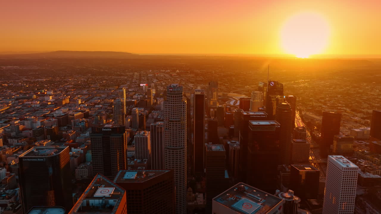 Los Angeles, EUA, 11 de janeiro de 2026: Vista aérea aproximada dos topos de arranha-céus durante um pôr do sol intenso. Vista detalhada dos telhados de edifícios do distrito financeiro com forte brilho solar e atmosfera alaranjada.