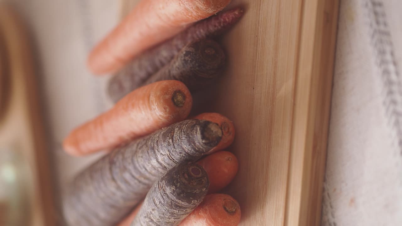 Carote fresche arancione e viola su una tavola da taglio di legno