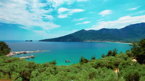 Aerial-View-From-A-Balcony-Slowly-Revealing-The-Iconic-Golden-Beach-With-Turquoise-Water,-Surrounded-By-Tall-Mountains,-Lush-Vegetation-And-A-Olive-Tree-Farm,-Thassos-Island,-Greece,-Europe