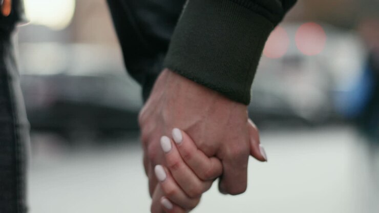 Close-up view of Caucasian hands of man and woman holding each other as they walk down the street