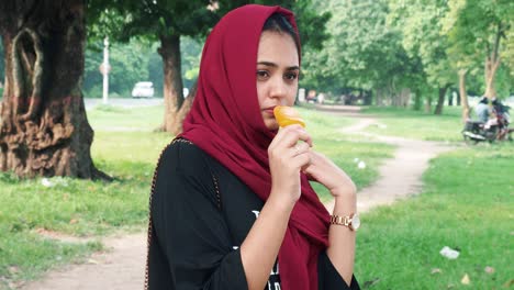 beautiful young afghan woman in hijab standing on lake and eats orange flavor ice cream