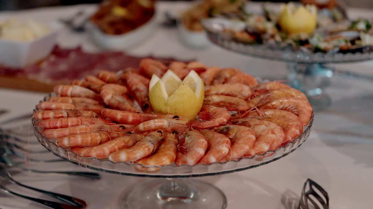 Cooked shrimp neatly arranged in a circle around a carved lemon on a glass serving dish