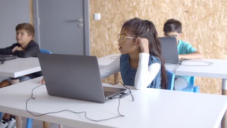 schoolchildren sitting at desks with laptops