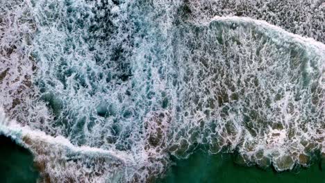 a view of the ocean from above of a cliff face with waves crashing on it