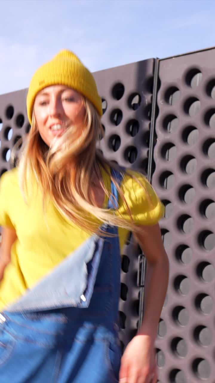 Woman in overalls dancing in front of a fence