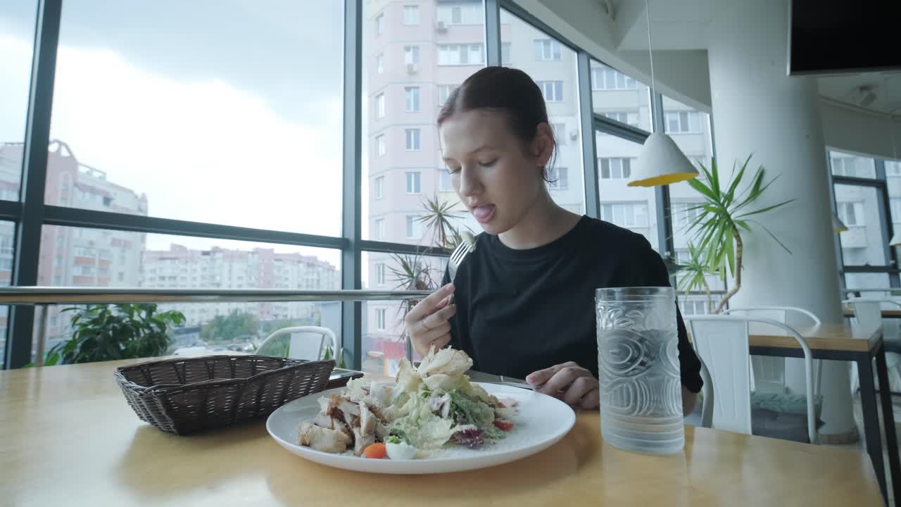 una mujer joven comiendo ensalada de césar en un restaurante moderno.