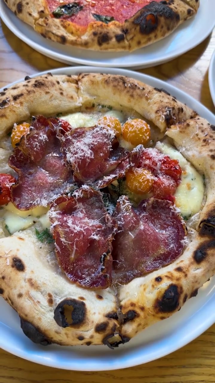 Vista ravvicinata dall'alto di pizze artigianali con crosta di pasta madre, salumi e pomodori freschi.