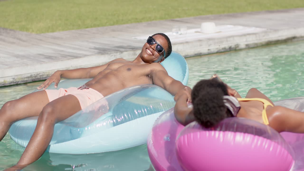Man reclining blue lounger, woman on pink donut float reaching and holding hands for lifestyle ads