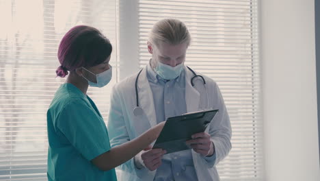 a young american nurse talks with a young doctor with long, blond hair, about medical results