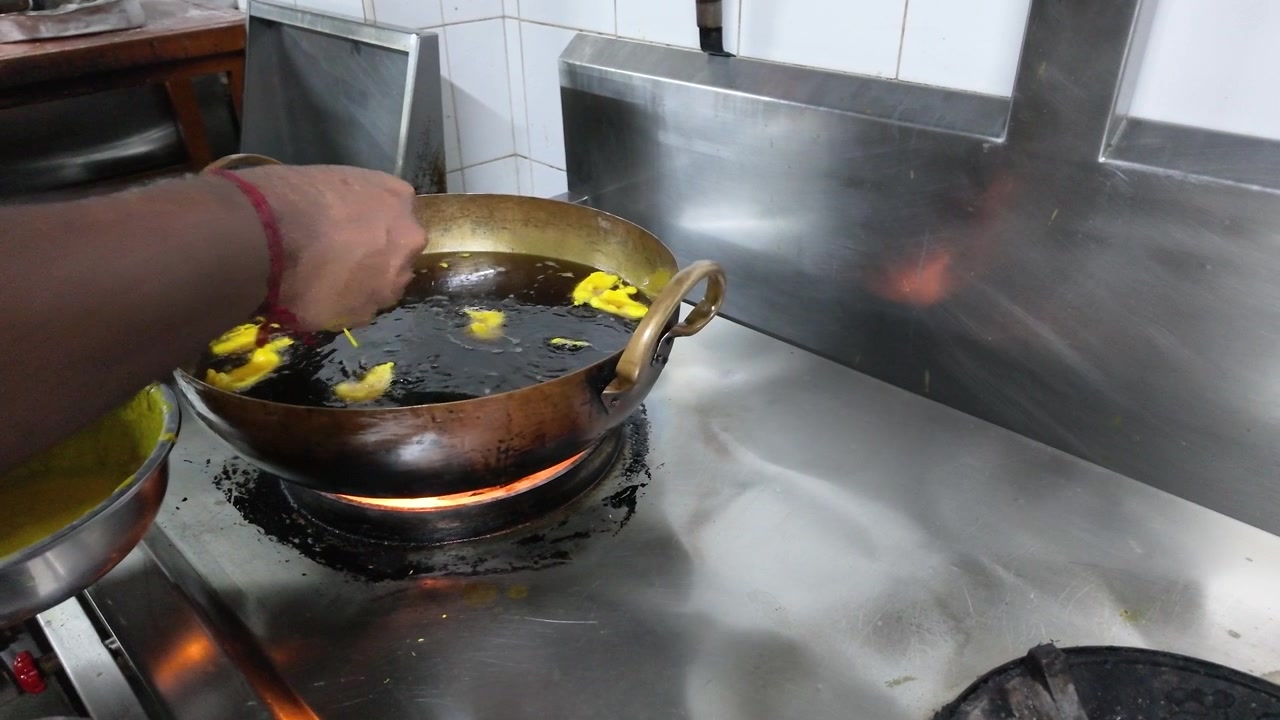 Close-up shot of hands dropping batter into hot oil for traditional Indian street food.