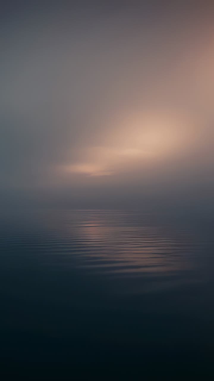 Vertical video: Glowing light nudging calm water shifting light band and ripples in mist at dawn