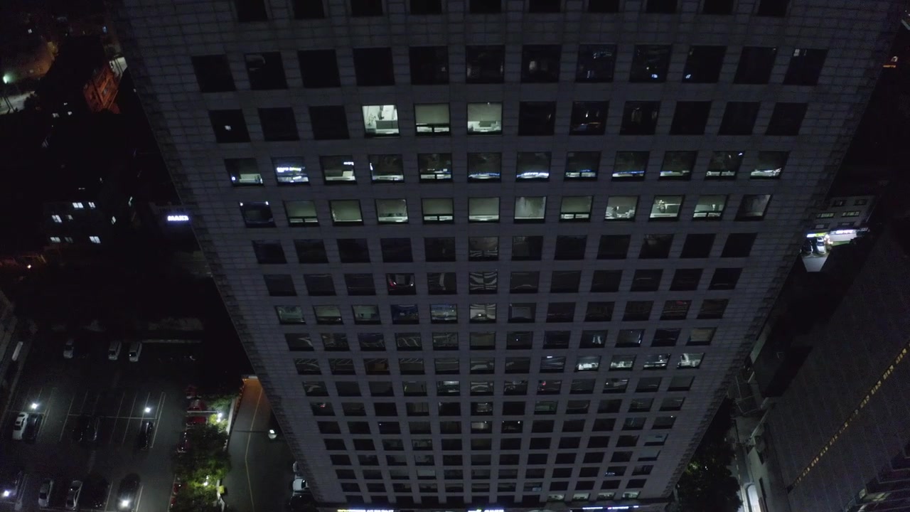 Un alto edificio de oficinas se alza sobre una concurrida calle de la ciudad al anochecer, mientras coches y autobuses circulan por debajo en línea recta.
