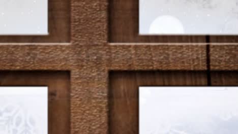 Christmas-tree-and-wooden-window-frame-against-snow-falling-over-multiple-trees-on-winter-landscape