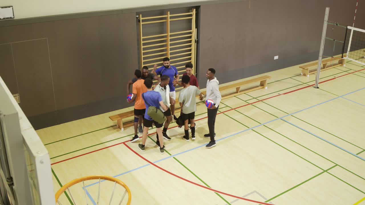 Divers mannenteam arriveert met sporttassen en volleybal, vormt een kring bij de training in de schoolgymzaal.