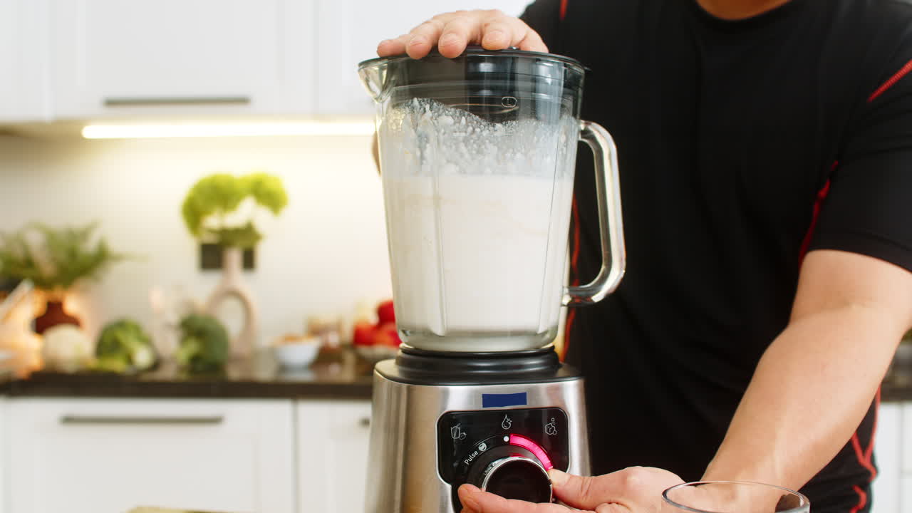 Uomo che usa un frullatore in una cucina di casa per preparare un frullato sano con banana, latte, ricotta e proteine del siero del latte