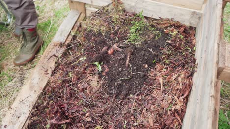 gardener filling raised garden bed with compost pile