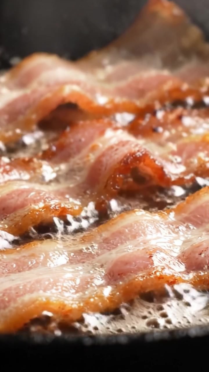 Sprøde strimler af sprød bacon, der steger på en pande, viser den lækre gyldenbrune tekstur, mens den tilberedes i varm olie, hvilket skaber mundvandsløbende aromaer og en lækker morgenmadsfavorit.