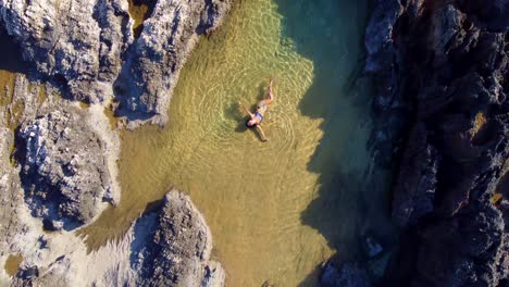 Girl-laying-in-a-salt-pool-in-rocks-next-to-sea