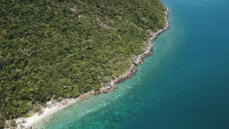 Drone-aerial-pan-up-of-tropical-island-with-clear-blue-water-with-a-green-forest