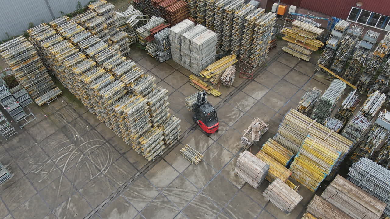 Aerial of a forklift truck driving through high stacks of construction materials on an industrial storage yard