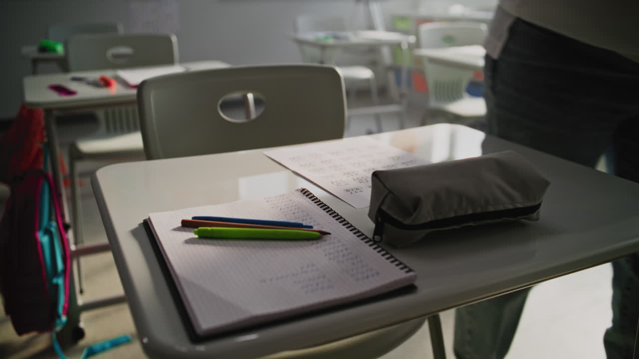 Female Teacher Placing Sheets of Paper with Writing Tasks on Students Desks