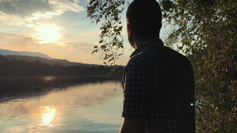 un hombre se acerca al borde del lago recortado contra una puesta de sol dorada