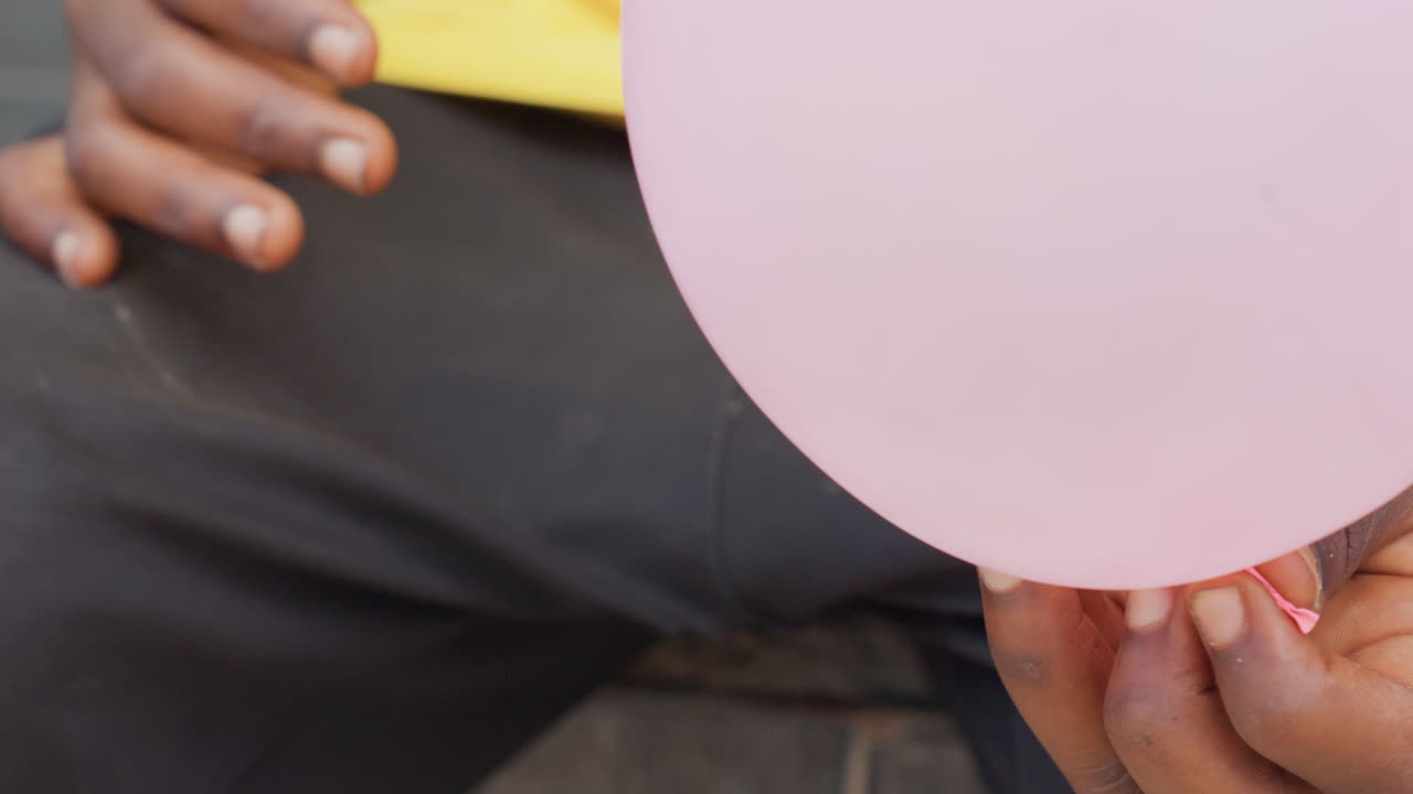 Un bambino assicura un palloncino rosa. Il bambino annoda delicatamente un piccolo palloncino rosa con attenzione concentrata. Un bambino che indossa il giallo assicura meticolosamente il palloncino rosa con movimenti delicati e attenti.