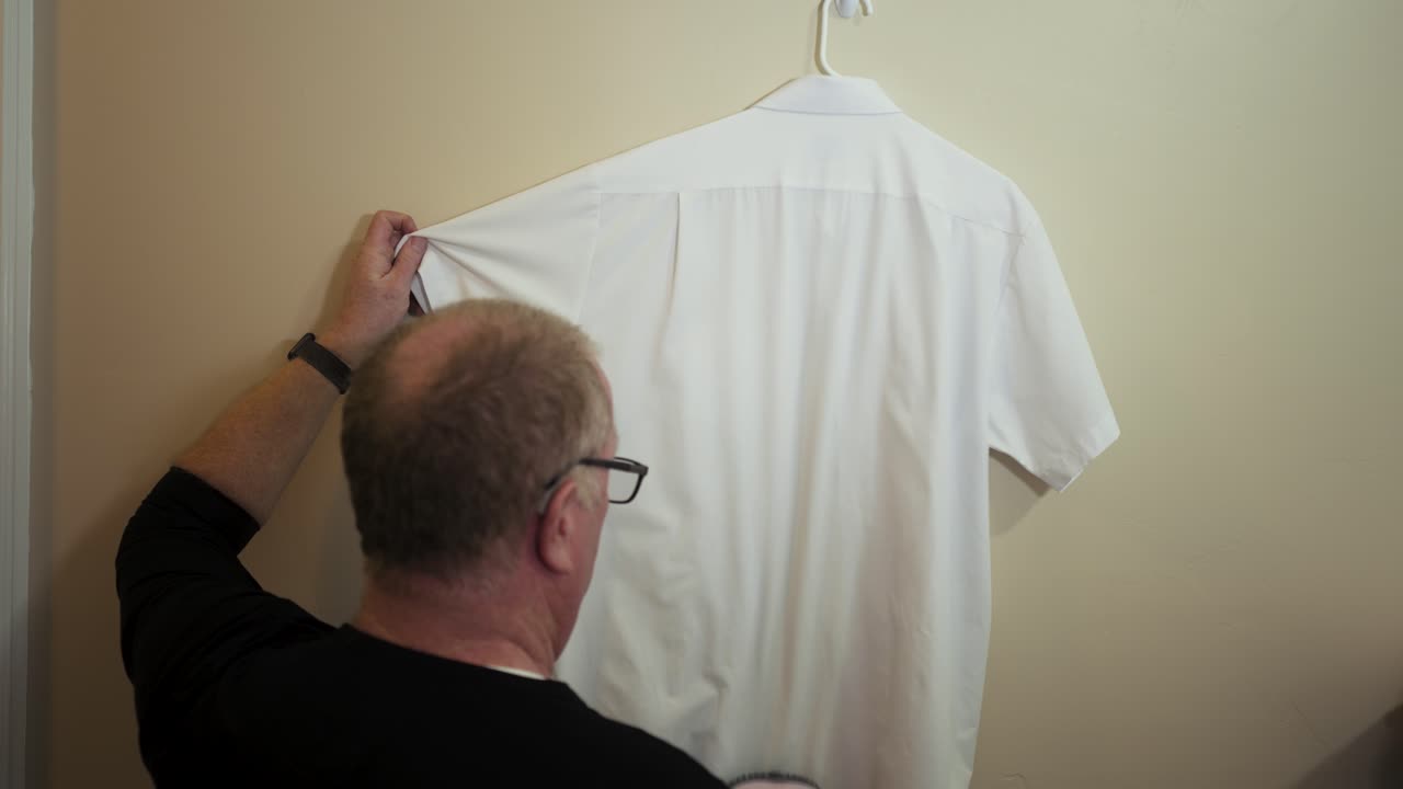 Man removing wrinkles from a white shirt using a fabric steamer