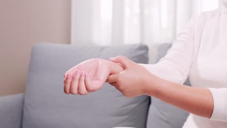 a woman in a white shirt sits on the sofa and massages her arms and wrists