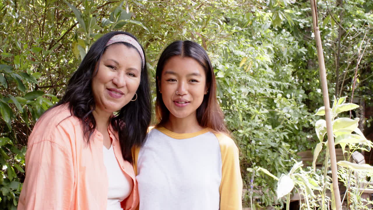 Smiling multiracial grandmother and young woman enjoying time together in lush garden, copy space