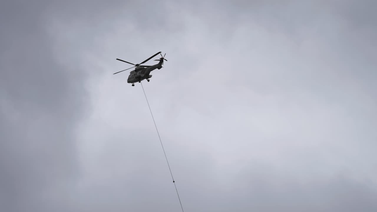 helicóptero de carga con cable de elevación y carga conectada haciendo una entrega en el terreno montañoso de difícil acceso
