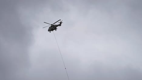 cargo helicopter with lifting cable and load attached making a delivery in the difficult-to-reach mountainous terrain