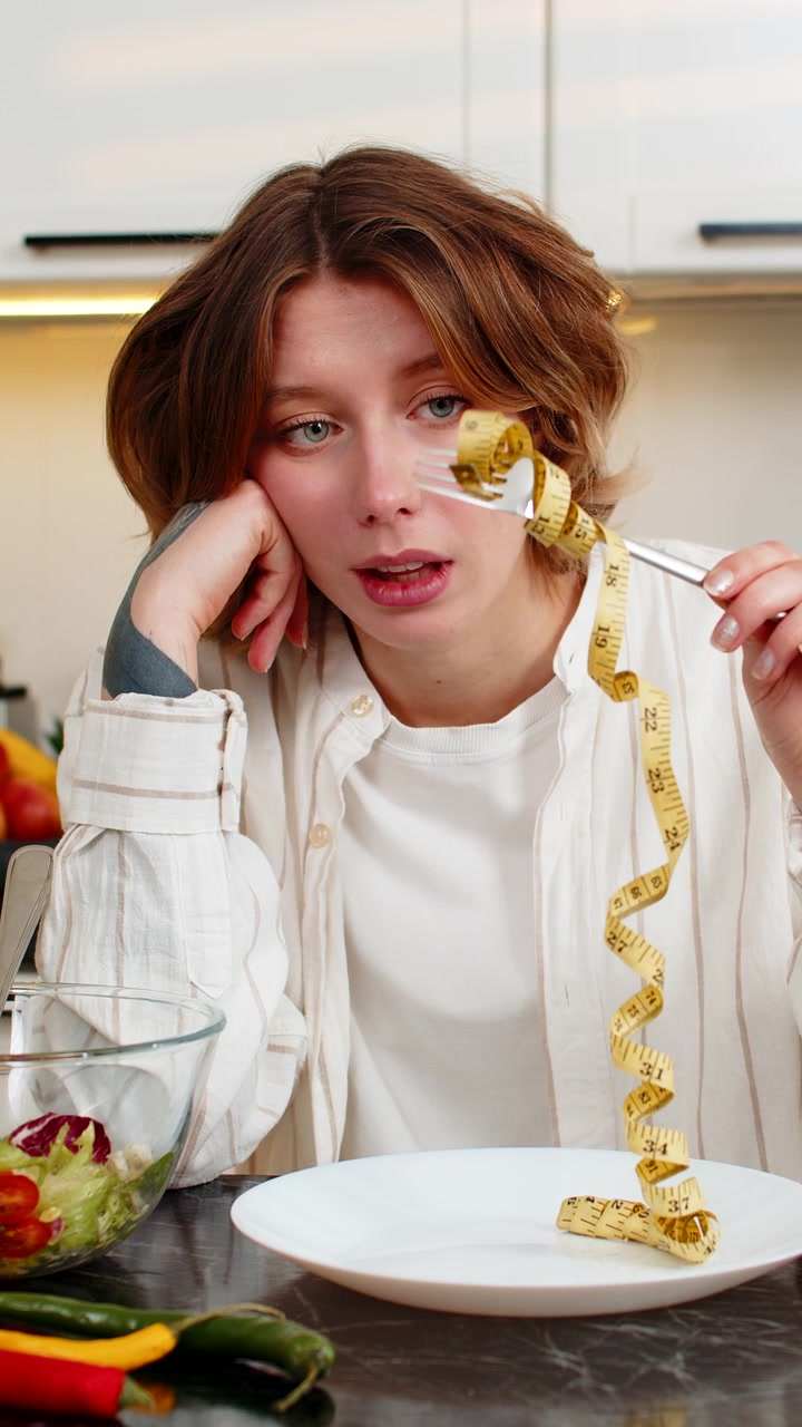 Eine junge Frau ist in ihrer heimischen Küche verstimmt, während sie eine Diät macht und über Gewichtsverlust und gesunde Ernährung nachdenkt.