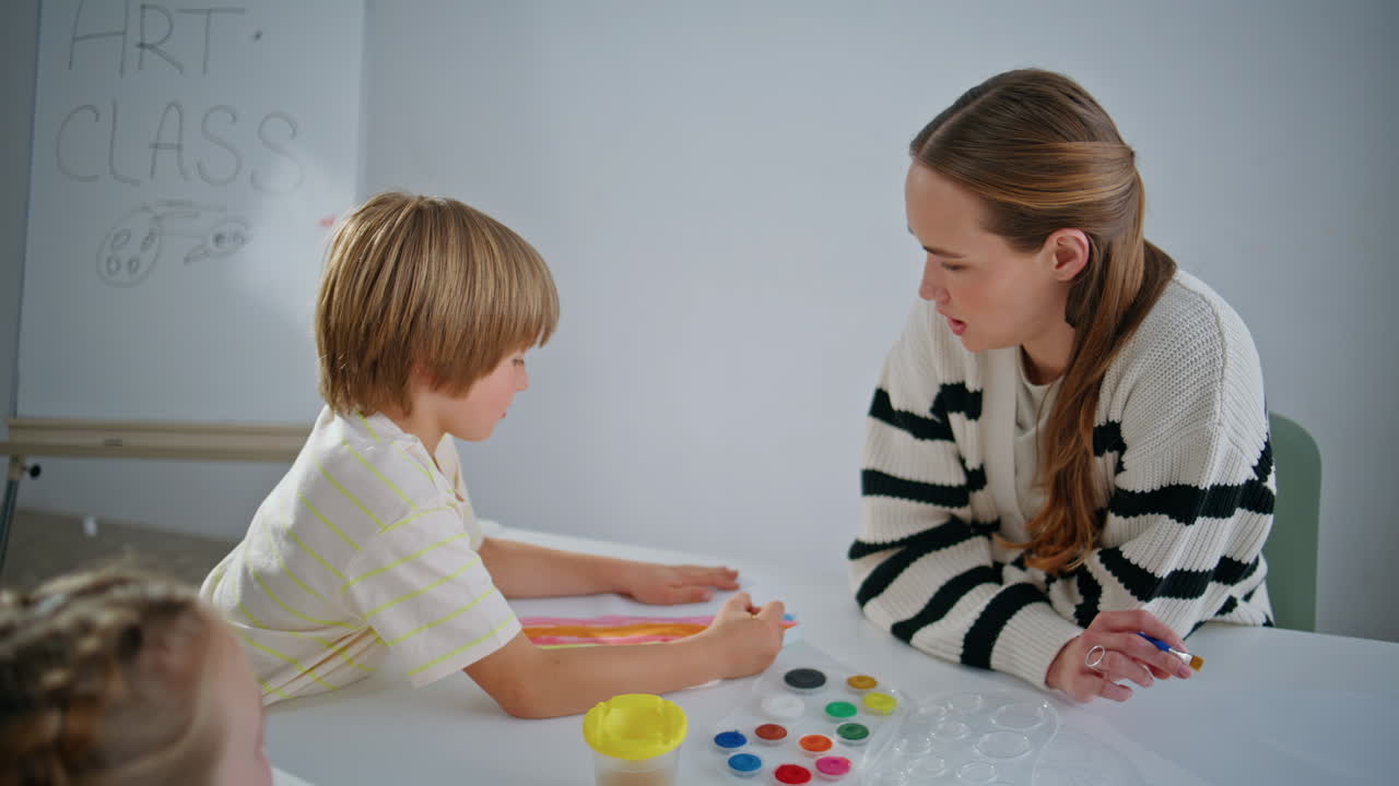Focused teacher boy painting on paper with paintbrushes in art studio closeup