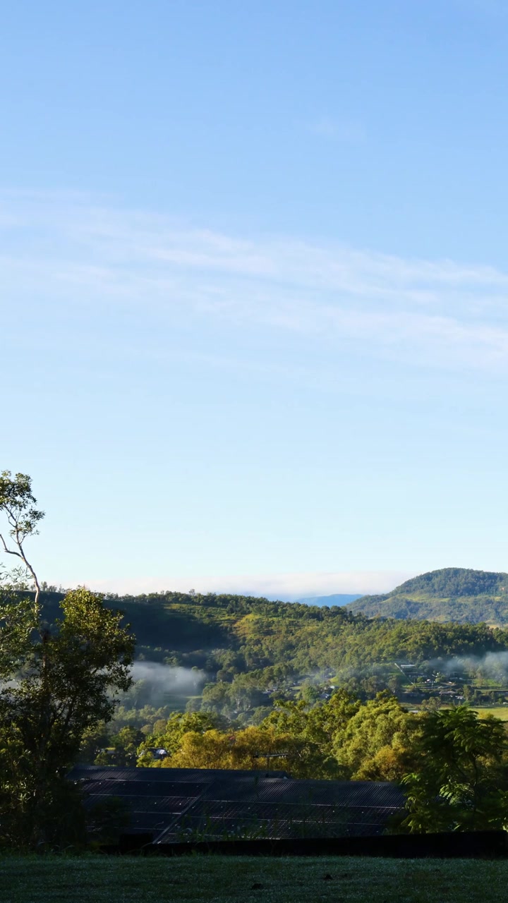En fredfyldt lodret udsigt over tåge, der letter over skovklædte bjerge under en klar blå himmel.