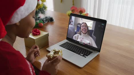 Mujer-Afroamericana-Con-Gorro-De-Papá-Noel-Usando-Una-Computadora-Portátil-Para-Una-Videollamada-Navideña,-Con-Un-Amigo-En-La-Pantalla