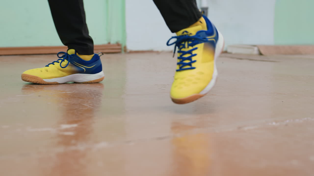 Lower angle close up of athlete wearing yellow blue sports shoes practicing footwork during indoor training session, showing movement, agility, and balance on fast steps and active performance