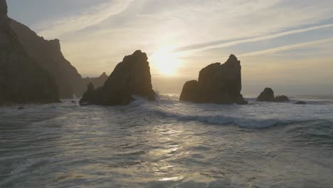 Aerial-view-reaching-rocky-cliffs-on-Atlantic-Ocean-at-Ursa-Beach,-cloudy-sunset-in-Portugal